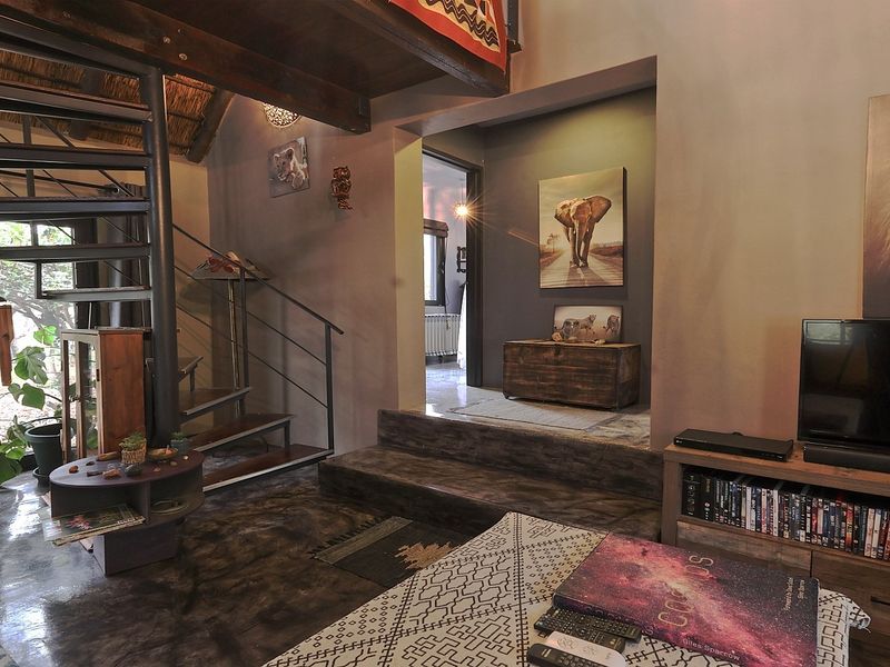 Living area featuring a distinctive spiral staircase, exposed timber beams, thatched ceiling, and polished concrete flooring with a raised transition to the adjacent room.