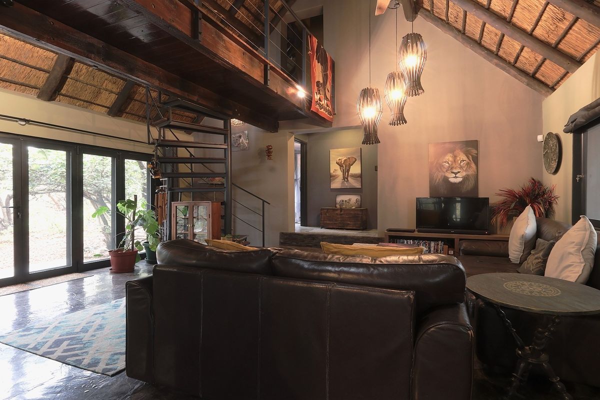 Spacious living room featuring a high exposed thatch ceiling, mezzanine level with a spiral staircase, and large sliding glass doors opening to the outdoors.
