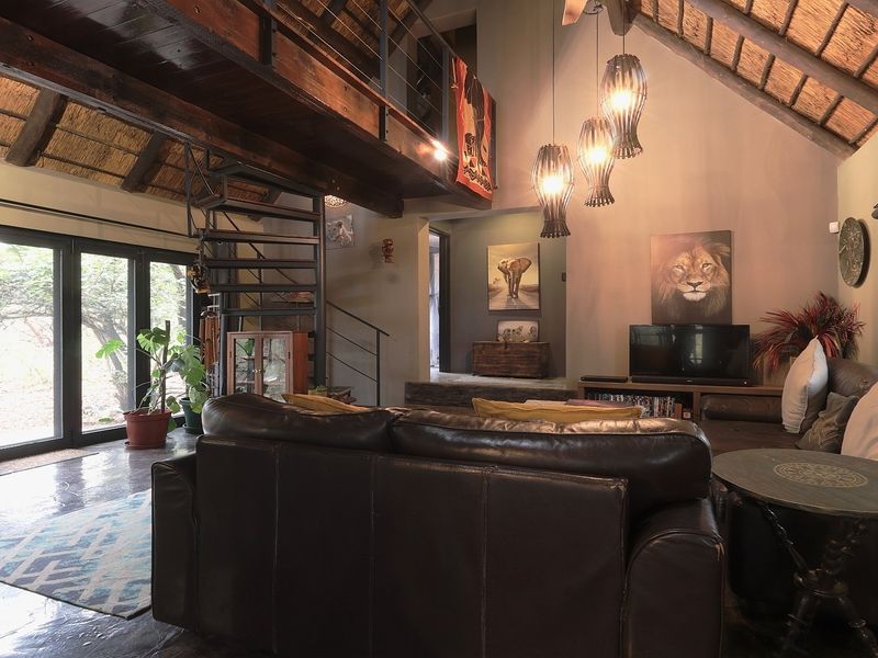 Spacious living room featuring a high exposed thatch ceiling, mezzanine level with a spiral staircase, and large sliding glass doors opening to the outdoors.
