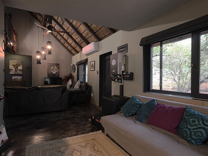 A cozy living area featuring a high thatched ceiling with exposed rafters, dark concrete floors, and integrated solar power infrastructure.