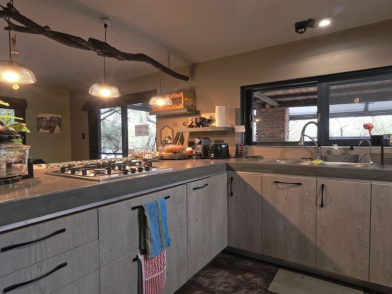 Modern kitchen featuring concrete countertops, light wood-grain cabinetry, a gas hob, and an undermount sink with a view of the outdoor area.