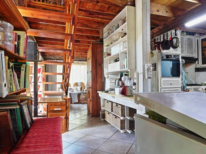 Open-plan kitchen and living area featuring exposed timber ceilings, a wooden staircase, and tiled flooring, offering a rustic and functional layout.