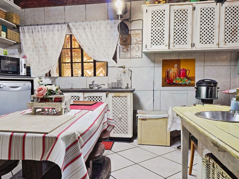 A dated kitchen featuring tiled walls, built-in cabinetry, double sink, and exposed timber ceiling beams, offering significant potential for a modern renovation.