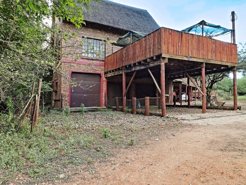 Rear view of a facebrick house featuring a thatched roof, integrated garage doors, and an elevated timber deck structure.