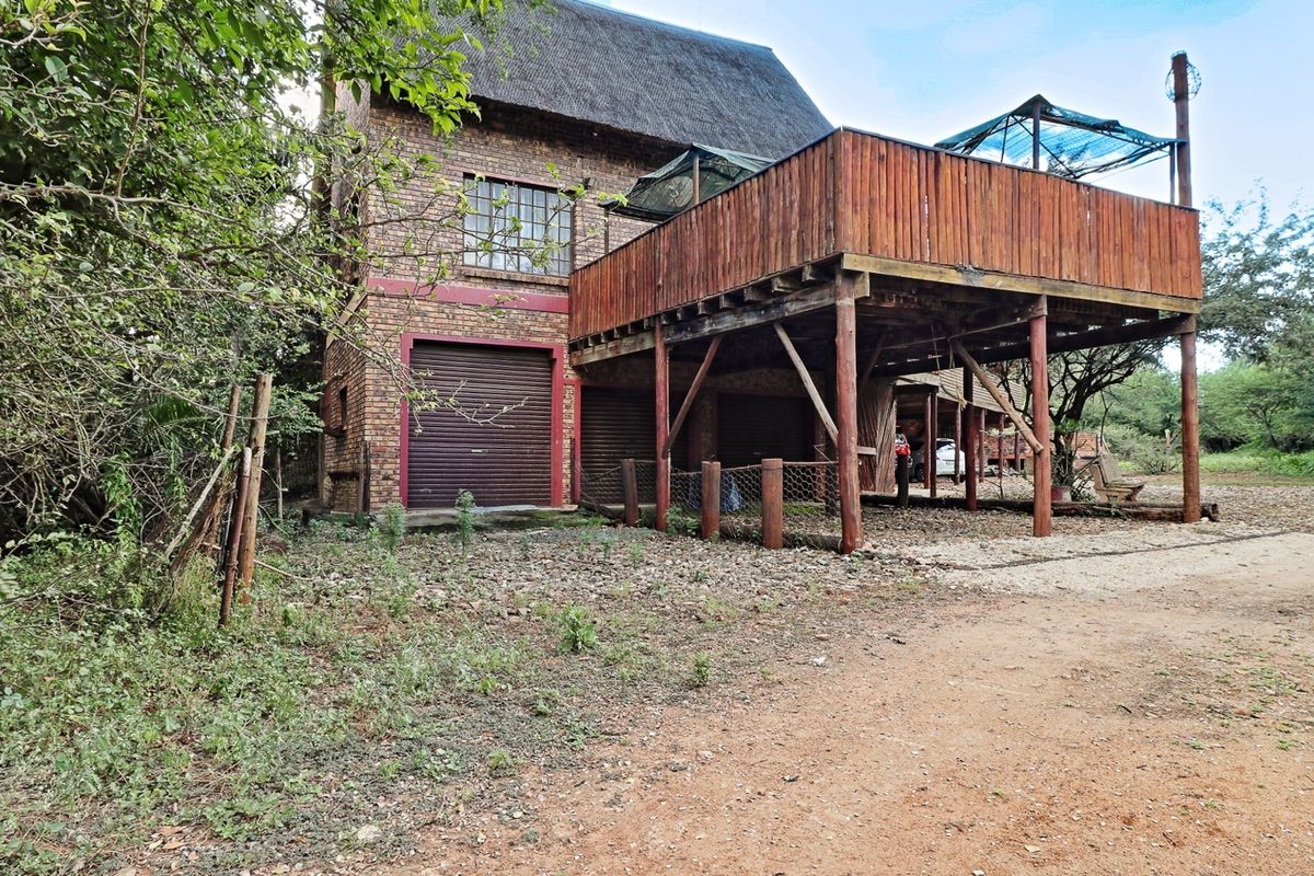 Rear view of a facebrick house featuring a thatched roof, integrated garage doors, and an elevated timber deck structure.