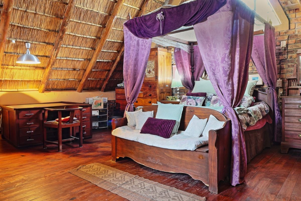 A rustic bedroom featuring an exposed thatch roof, timber flooring, and exposed brick walls, creating a warm and character-filled living space.
