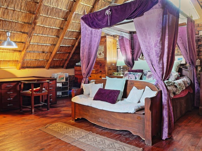 A rustic bedroom featuring an exposed thatch roof, timber flooring, and exposed brick walls, creating a warm and character-filled living space.