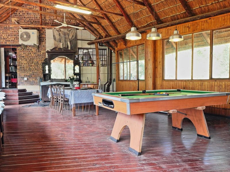 Spacious living area featuring a high thatched ceiling with exposed timber trusses, brick walls, timber paneling, and polished timber flooring.