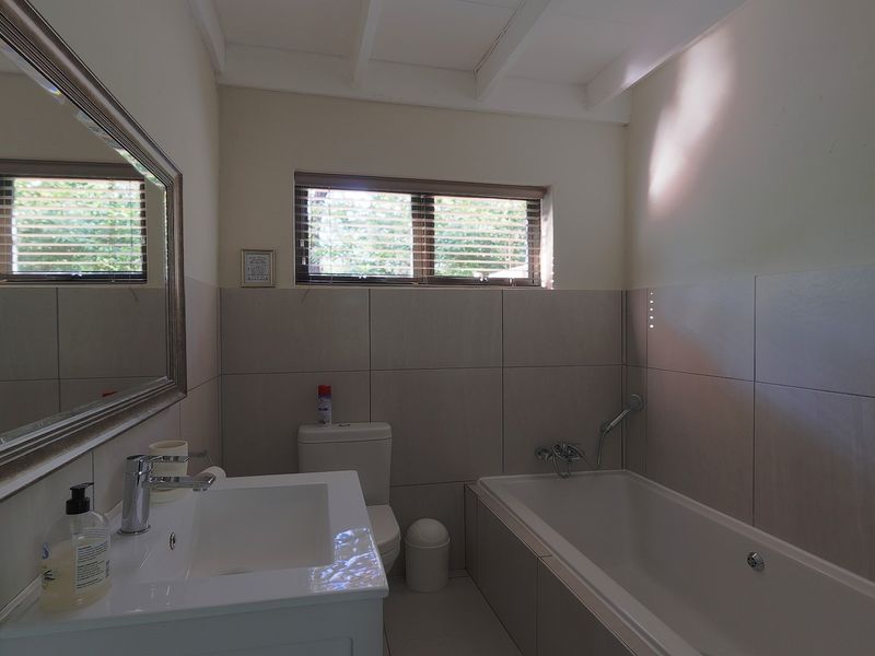 A functional bathroom featuring a vanity basin, bathtub with shower mixer, and neutral wall tiling, providing a clean and practical space.