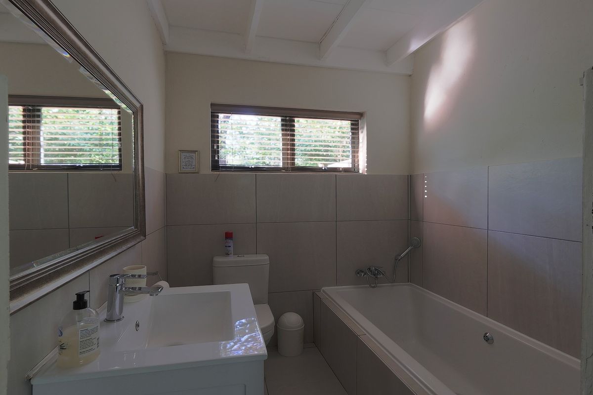 A functional bathroom featuring a vanity basin, bathtub with shower mixer, and neutral wall tiling, providing a clean and practical space.