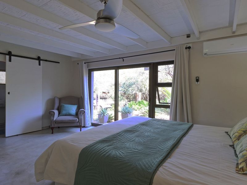 Spacious bedroom featuring exposed beam ceilings, a ceiling fan, split-system air conditioning, and a sliding glass door providing access to the garden.