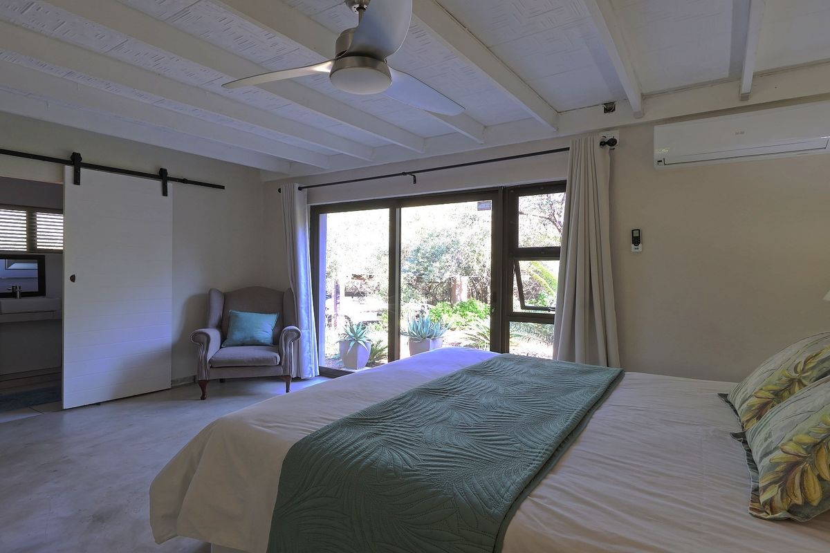 Spacious bedroom featuring exposed beam ceilings, a ceiling fan, split-system air conditioning, and a sliding glass door providing access to the garden.