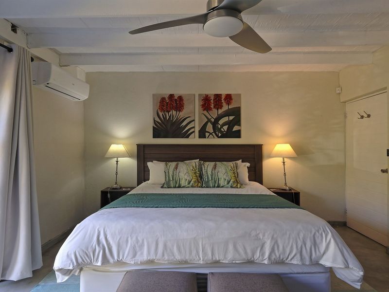 A well-maintained bedroom featuring exposed beam ceilings, a split-system air conditioner, and a ceiling fan, with direct access to an outdoor area.