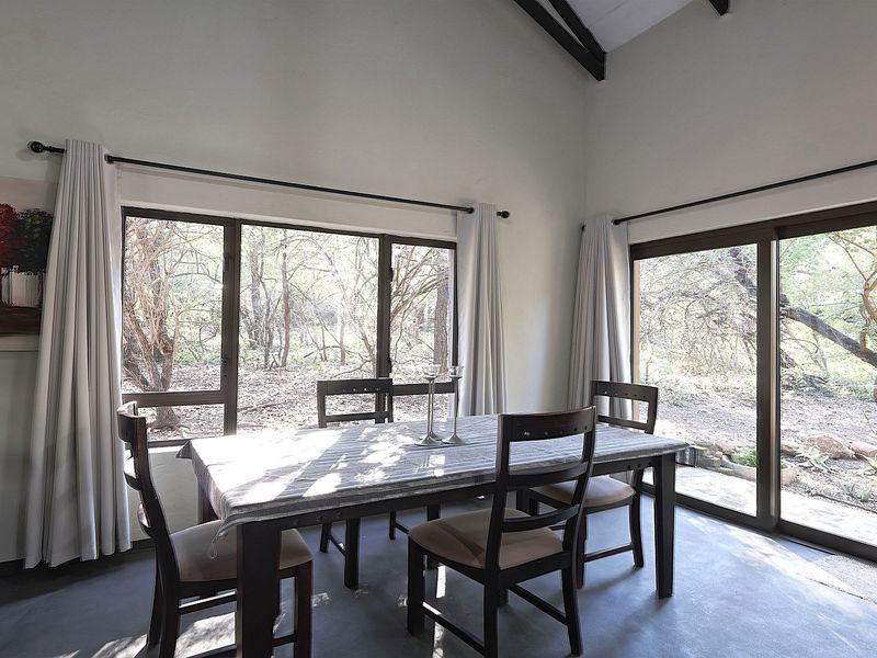 Bright dining area featuring exposed timber ceiling beams, concrete flooring, and large windows providing scenic views of the surrounding natural landscape.