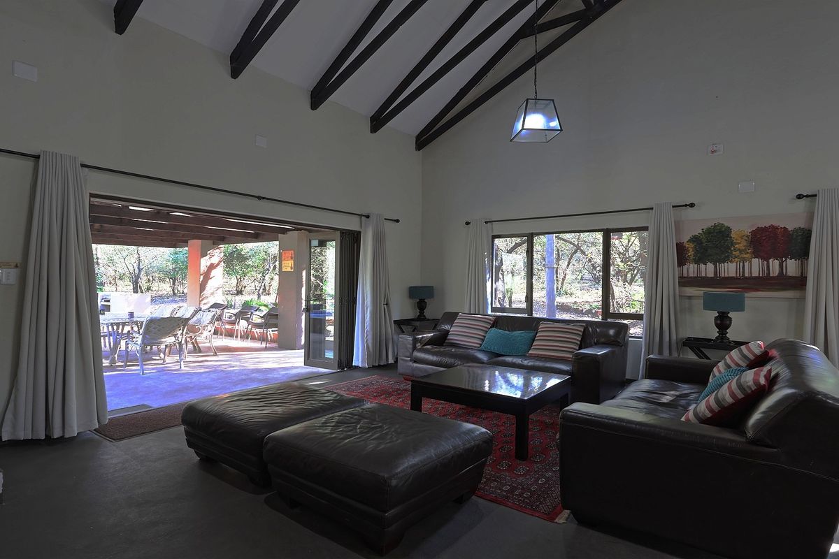 Spacious living room featuring a high vaulted ceiling with exposed timber beams, large windows, and seamless access to an outdoor patio area.