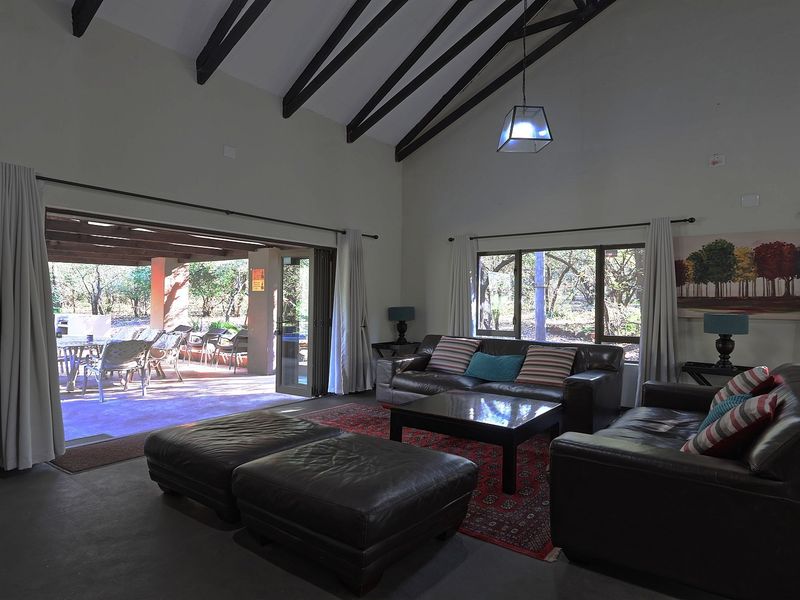 Spacious living room featuring a high vaulted ceiling with exposed timber beams, large windows, and seamless access to an outdoor patio area.