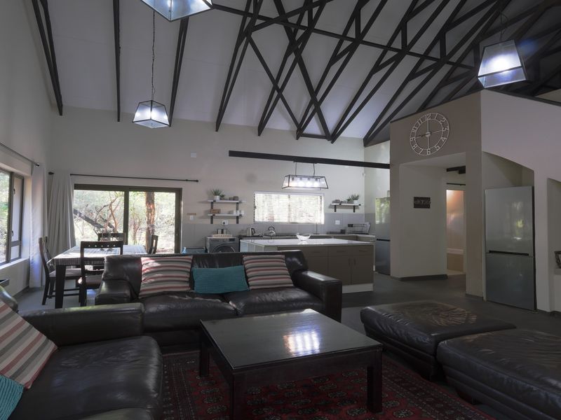 Spacious open-plan living and kitchen area featuring high vaulted ceilings with exposed timber trusses, tiled floors, and direct access to the outdoor space.