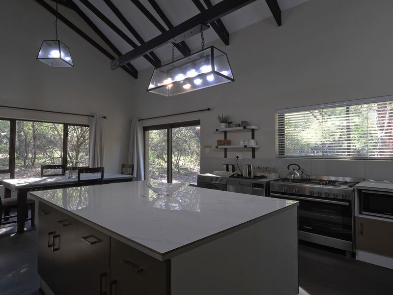 Spacious open-plan kitchen and dining area featuring exposed timber beams, a large central island with stone countertops, and direct access to the garden.