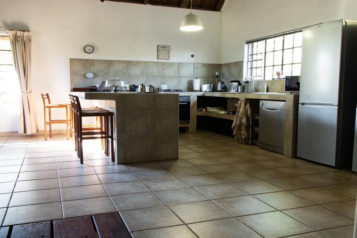 A spacious kitchen featuring tiled flooring, a central tiled island with breakfast bar seating, and ample counter space with a neutral tiled backsplash.
