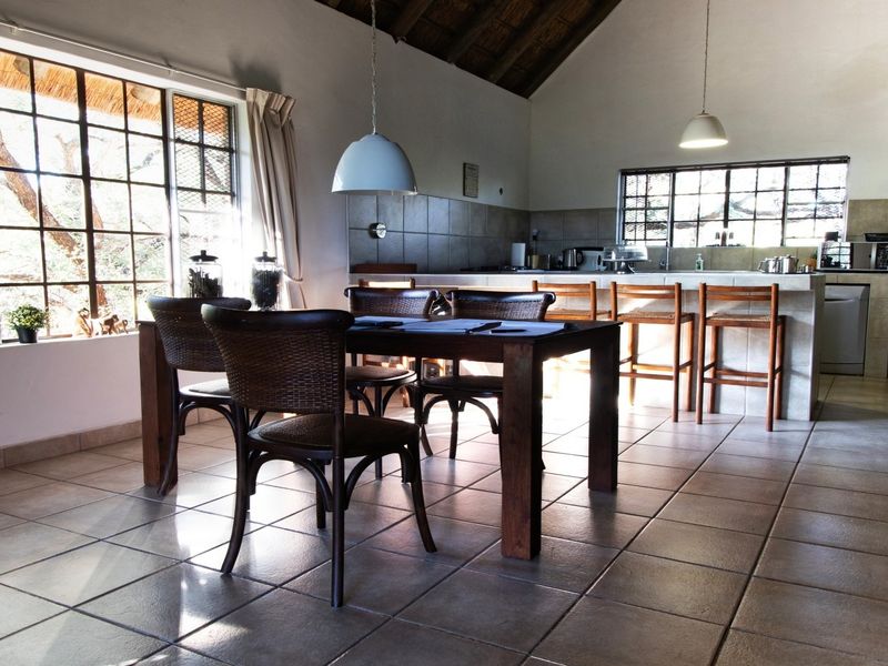 Spacious open-plan kitchen and dining area featuring vaulted ceilings with exposed beams, tiled flooring, and a functional kitchen island with breakfast bar seating.