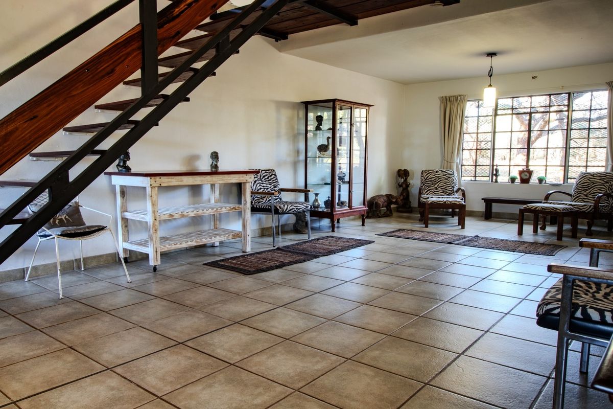 Spacious living area featuring tiled flooring and an open-tread staircase, with large windows providing natural light.