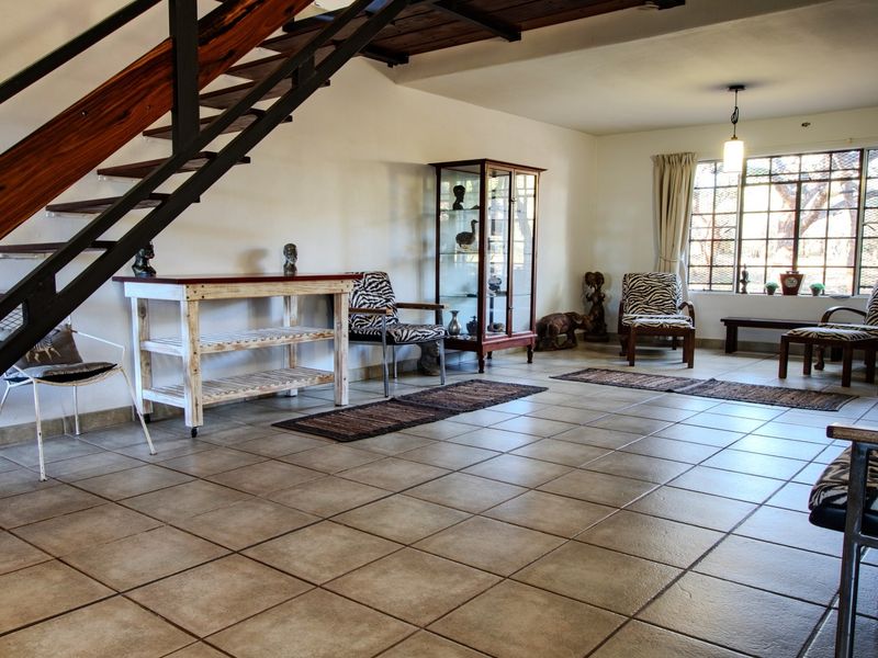 Spacious living area featuring tiled flooring and an open-tread staircase, with large windows providing natural light.