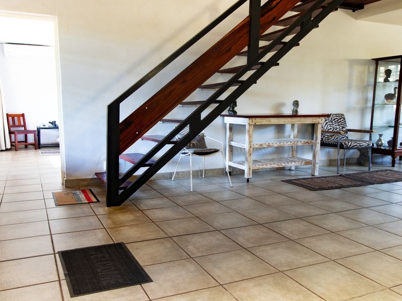Spacious living area featuring neutral tiled flooring and a modern open-tread staircase with metal and timber balustrades.