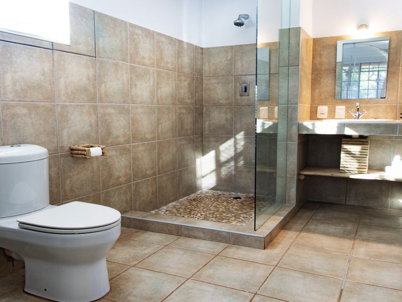 A well-maintained bathroom featuring a walk-in shower with a pebble floor, neutral ceramic tiling, and a built-in vanity with a wall-mounted mirror.