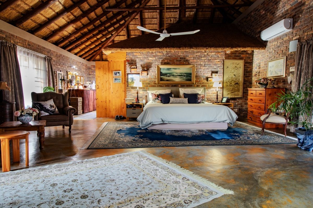 Spacious bedroom featuring rustic exposed brick walls, a high vaulted thatched ceiling, polished concrete floors, and integrated air conditioning.