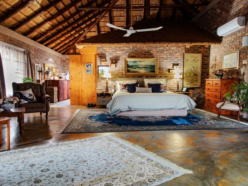Spacious bedroom featuring rustic exposed brick walls, a high vaulted thatched ceiling, polished concrete floors, and integrated air conditioning.