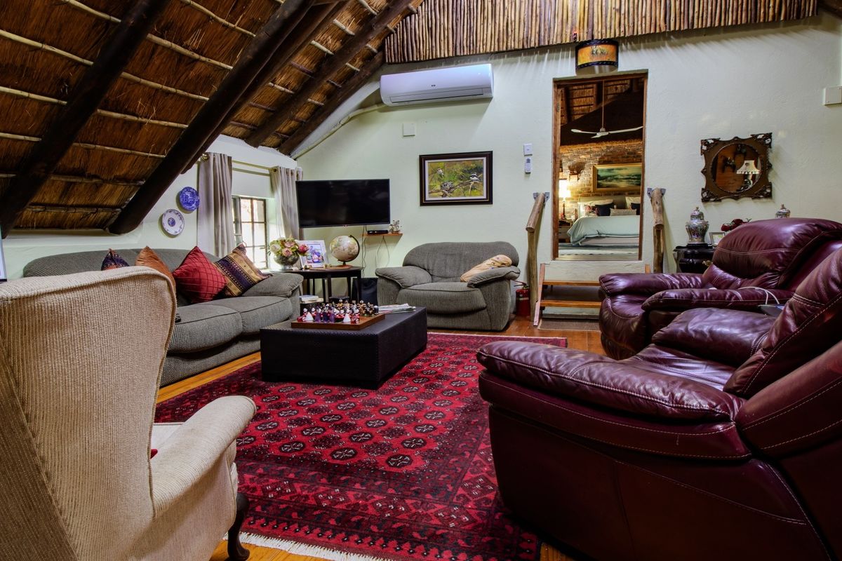 A cozy living room featuring a traditional thatched roof with exposed timber rafters, timber flooring, and a wall-mounted air conditioning unit.