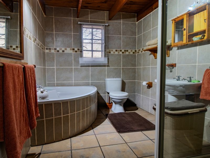 A bathroom featuring a corner bathtub, pedestal basin, toilet, and tiled finishes with exposed timber ceiling beams.