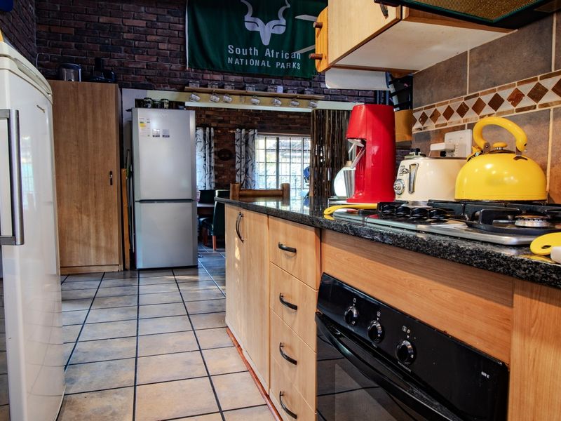 A functional kitchen featuring wooden cabinetry, granite countertops, a gas hob, and an exposed brick wall, offering a rustic aesthetic.