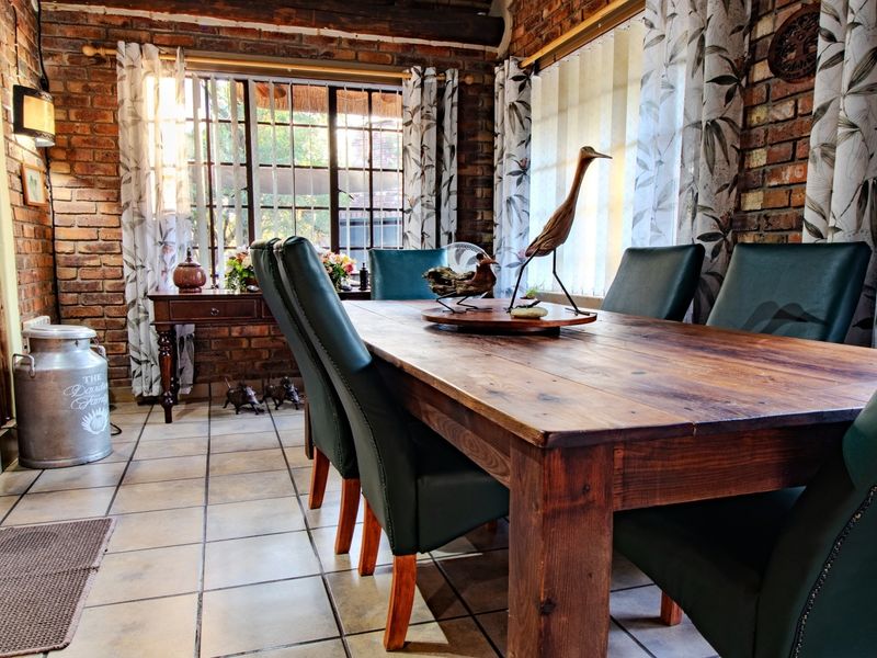 A rustic dining room featuring exposed brick walls, tiled flooring, and large windows that provide ample natural light.