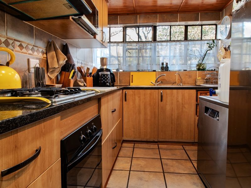 A functional kitchen featuring wood-finish cabinetry, granite countertops, a gas hob, built-in oven, and tiled backsplash with ample natural light.