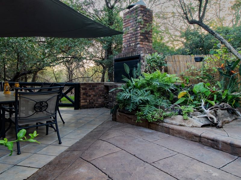 Outdoor patio area featuring a built-in brick fireplace, tiled flooring, and a landscaped garden border, providing a functional space for outdoor entertaining.