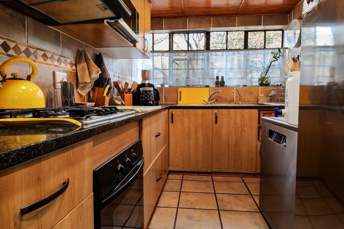 A functional kitchen featuring wood-finish cabinetry, granite countertops, a gas hob, built-in oven, and tiled backsplash with ample natural light.