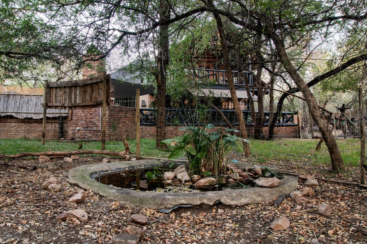 A view of the rear exterior of the house featuring a brick facade, a balcony, and a garden pond set within a wooded area.