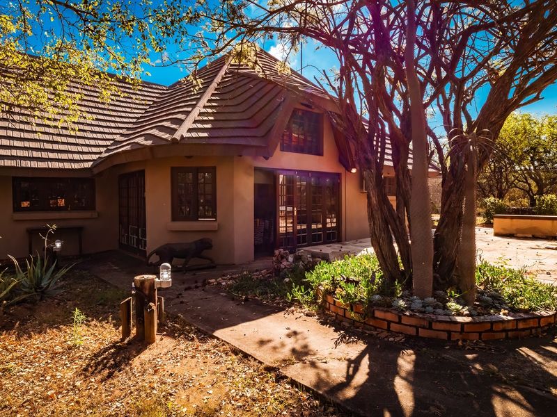 Rear exterior view of the house featuring a tiled roof, concrete patio area, and a built-in brick braai set within a garden.