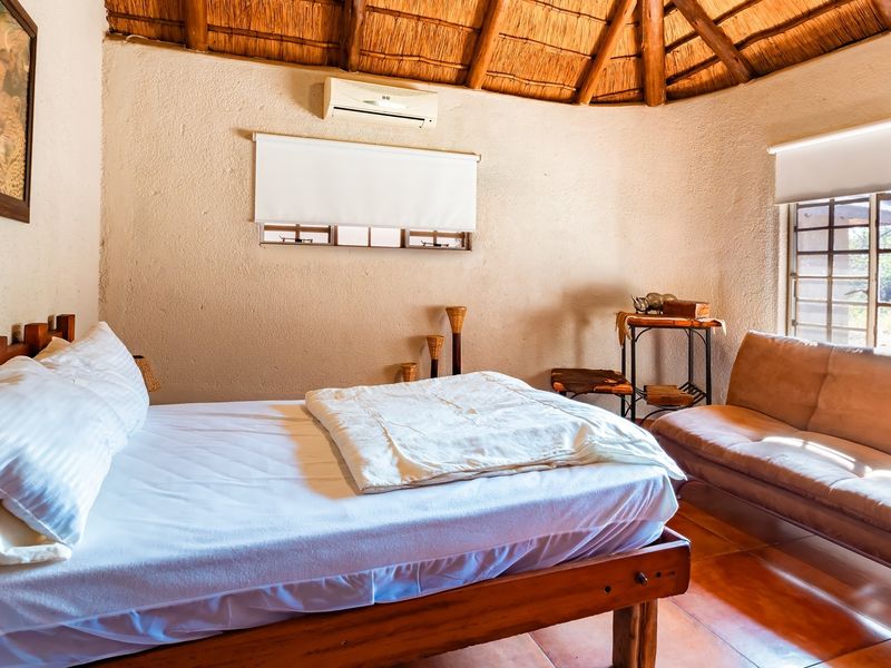A rustic bedroom featuring a traditional thatched roof with exposed timber rafters, tiled flooring, and a wall-mounted air conditioning unit.