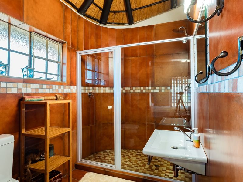 A bathroom featuring a shower enclosure, wall-mounted basin, and toilet, finished with distinctive orange wall tiles and a unique thatched ceiling.