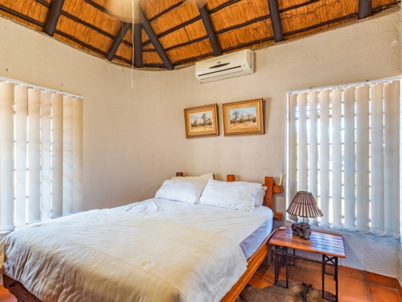 A cozy bedroom featuring a traditional thatched roof with exposed timber rafters, tiled flooring, and a wall-mounted air conditioning unit.