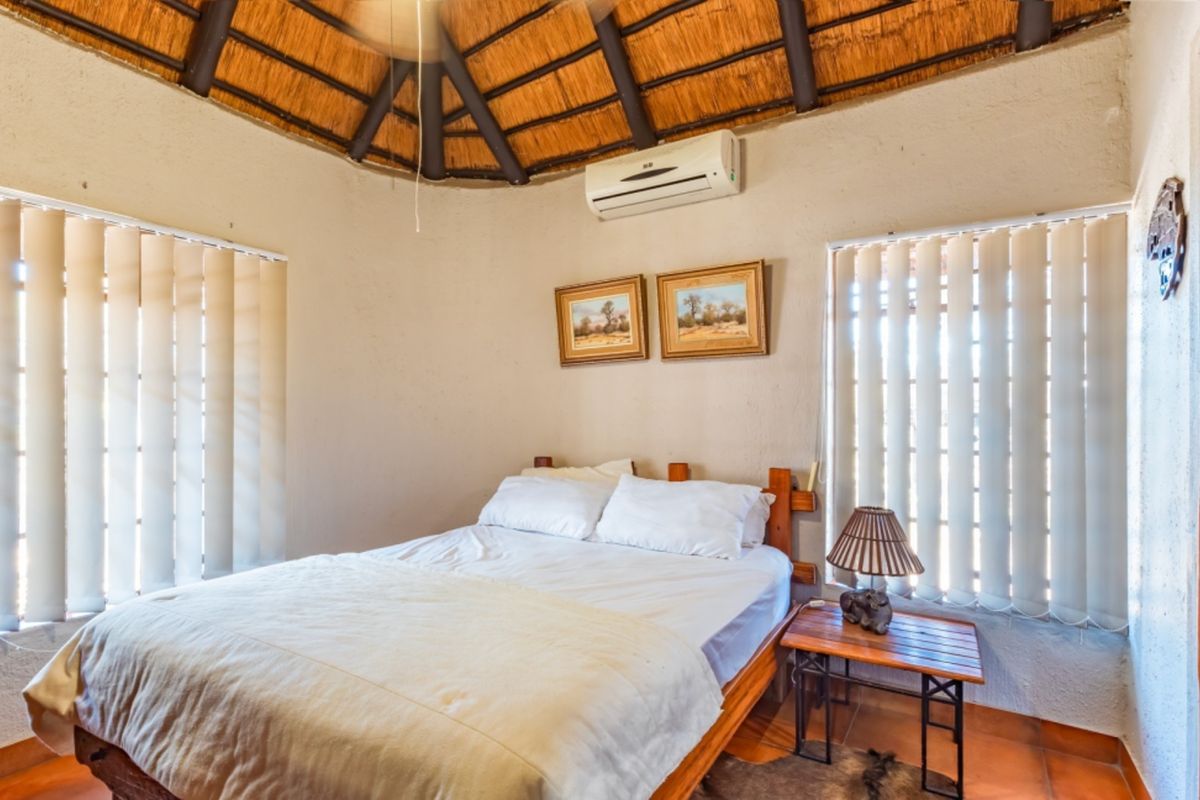 A cozy bedroom featuring a traditional thatched roof with exposed timber rafters, tiled flooring, and a wall-mounted air conditioning unit.