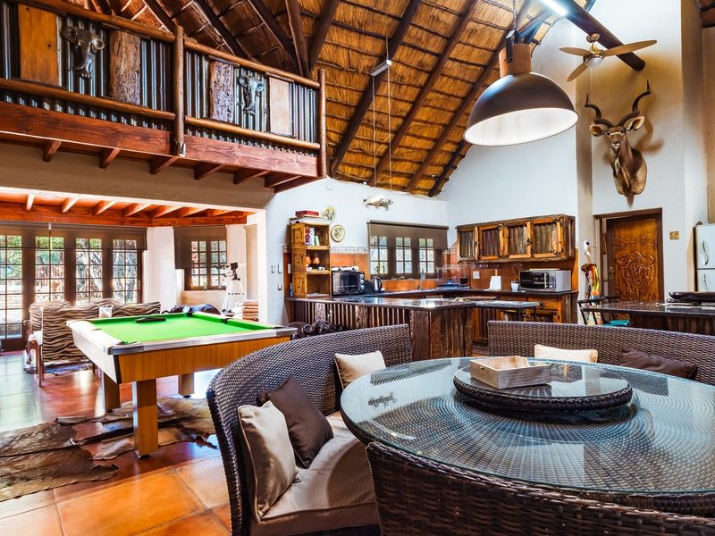 Spacious open-plan living and kitchen area featuring a high thatched ceiling, exposed timber beams, a mezzanine level, and rustic finishes throughout.