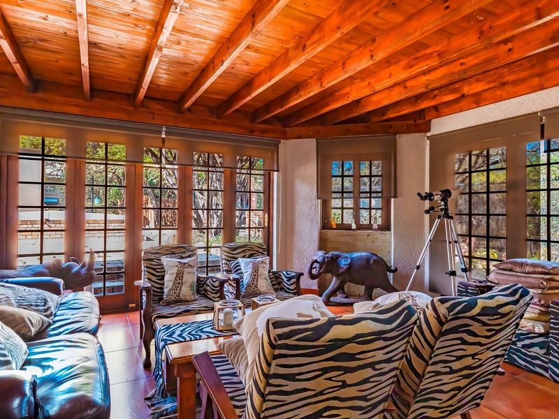 Spacious living area featuring a warm exposed timber beam ceiling, tiled flooring, and large glass doors that provide abundant natural light and garden views.