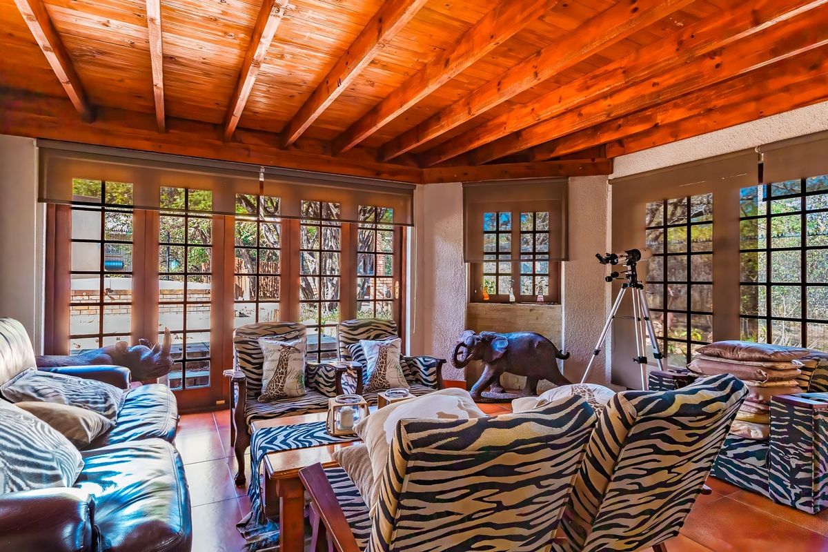Spacious living area featuring a warm exposed timber beam ceiling, tiled flooring, and large glass doors that provide abundant natural light and garden views.