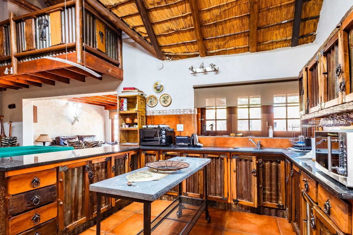 Rustic kitchen featuring custom wooden cabinetry, granite countertops, and a distinctive thatched roof with exposed timber beams, overlooking an adjacent living area.