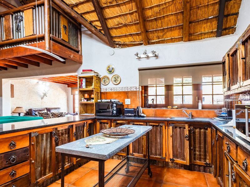 Rustic kitchen featuring custom wooden cabinetry, granite countertops, and a distinctive thatched roof with exposed timber beams, overlooking an adjacent living area.