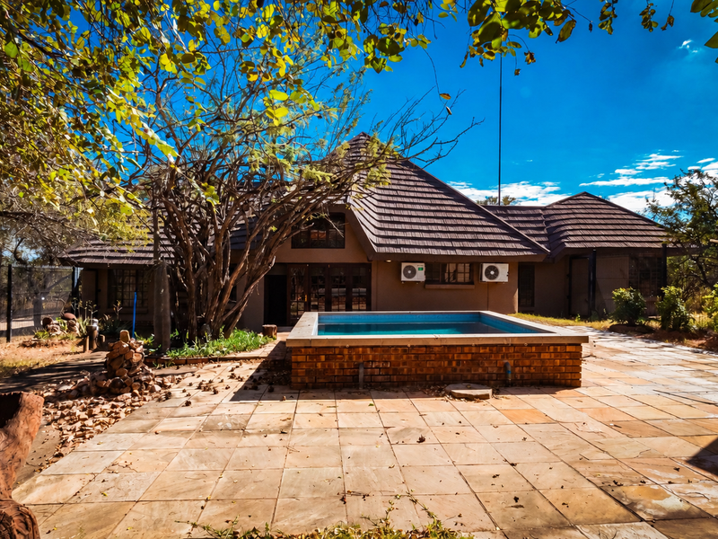Rear exterior view featuring a raised brick swimming pool, paved patio area, and a house with a tiled roof and wall-mounted air conditioning units.