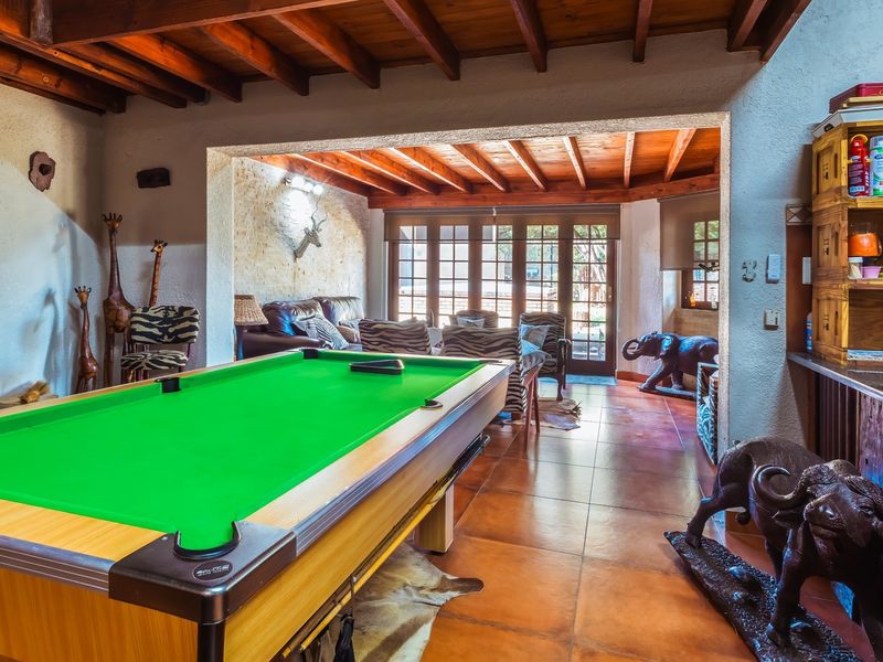 Spacious open-plan living area featuring exposed timber beam ceilings, tiled floors, and a stone feature wall, with direct access to the outdoors via french doors.